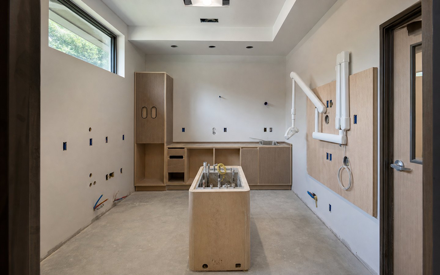 Medical and Dental Office Remodeling during planning visualization of the same space: The centered chair utility box, rear casework and sink, storage tower, equipment backing, and task-light rough-ins establish the clinical layout.